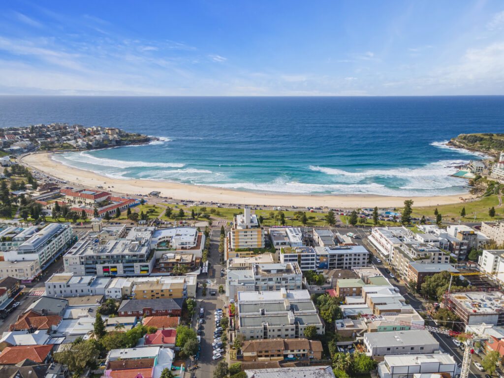 Drone photo of a beachside suburb with the ocean and a curved sandy beach